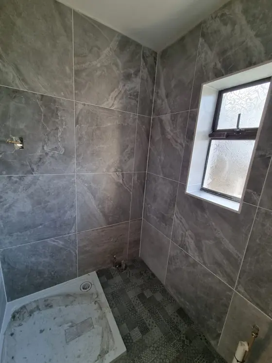 Large-format grey tiles installed in a shower room with new shower tray
